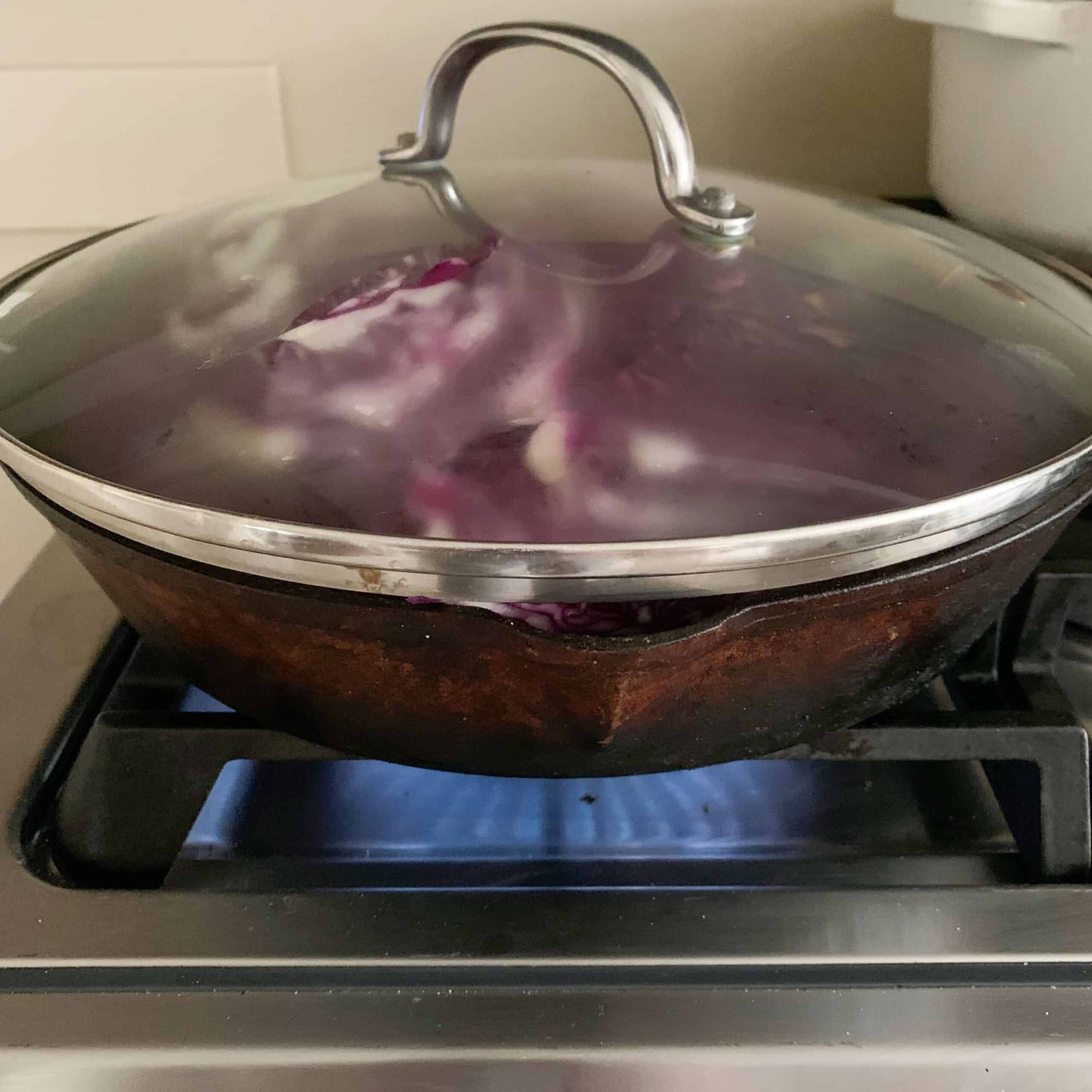 covered cast iron pan with cabbage inside cooking on stove