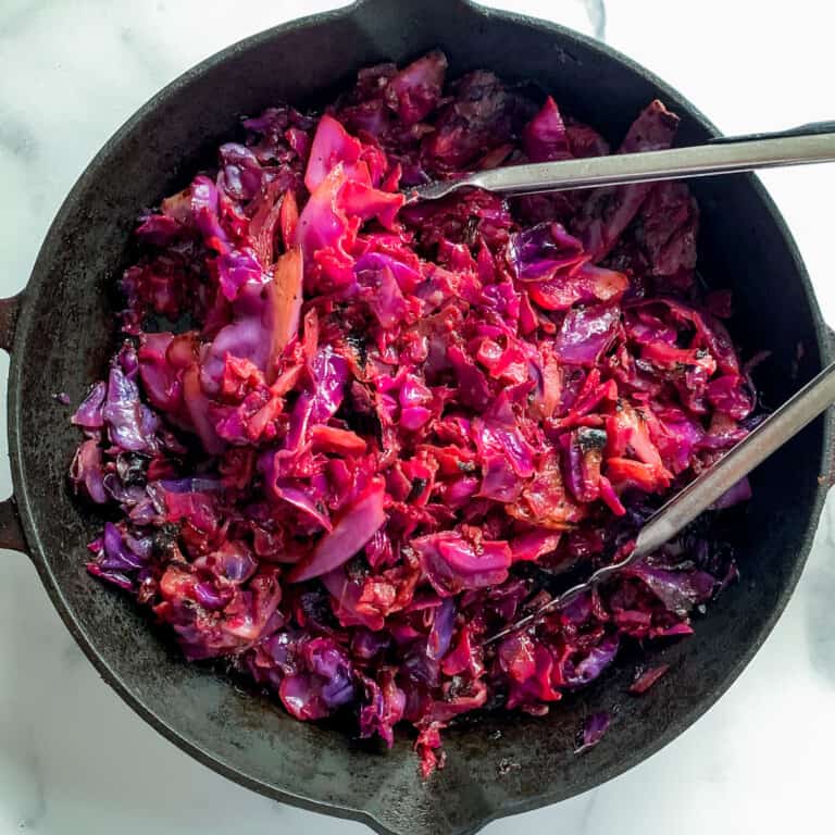 top view of roasted red cabbage in cast iron pan with tongs