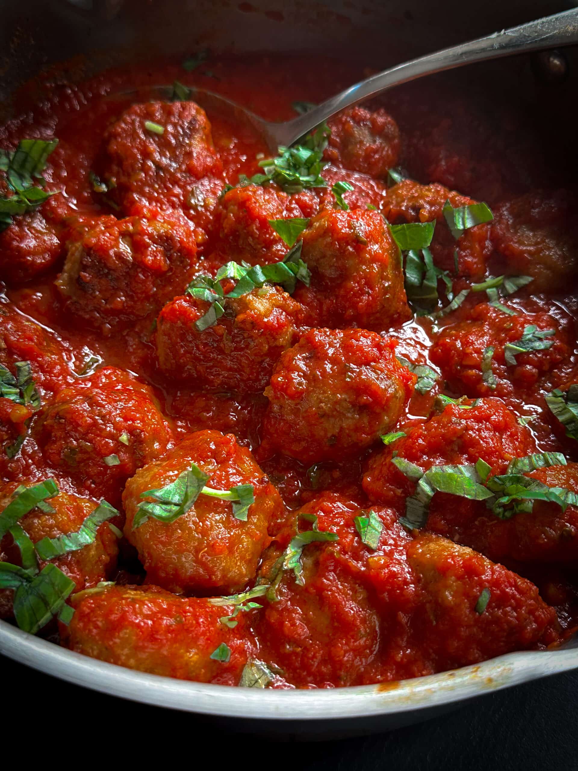 Italian meatballs in sauce in silver pan with large spoon