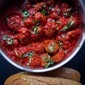 top view of Italian meatballs in tomato sauce in bowl with seeded bread