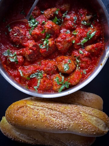 top view of pan of meatballs with sauce and rolls on side