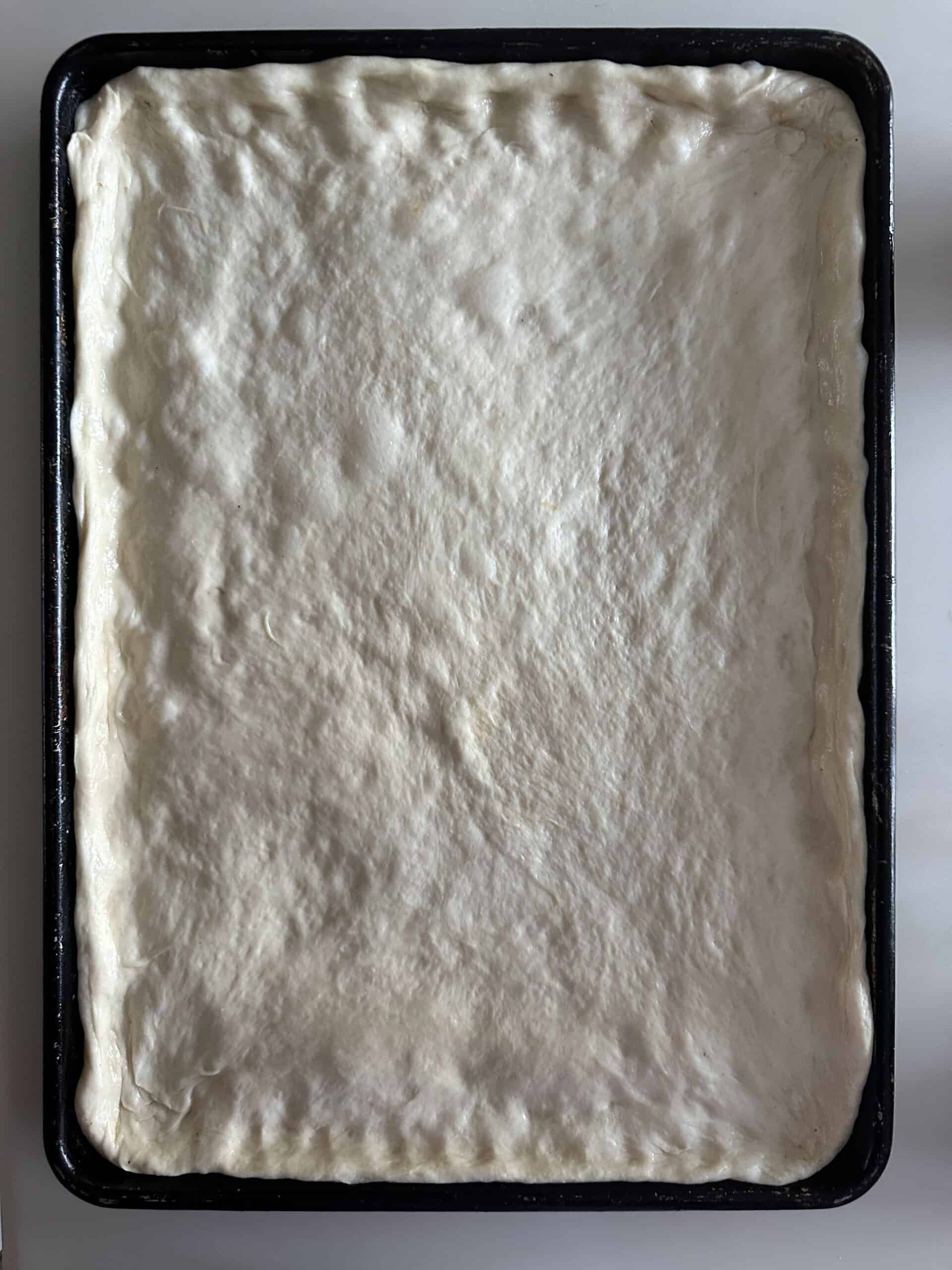 pizza dough stretched out in half sheet pan