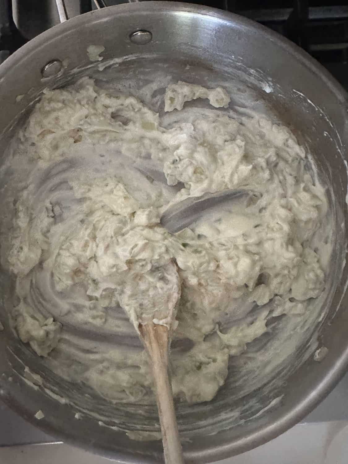 Cream cheese and cream added to vegetables in pan with spoon 