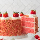 strawberry crunch cake on white cake pedestal with slice being removed