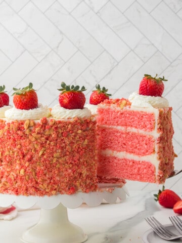 strawberry crunch cake on white cake pedestal with slice being removed