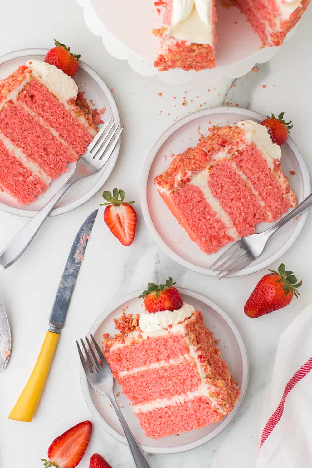 three slices of strawberry cake with fresh strawberries on white plates with forks