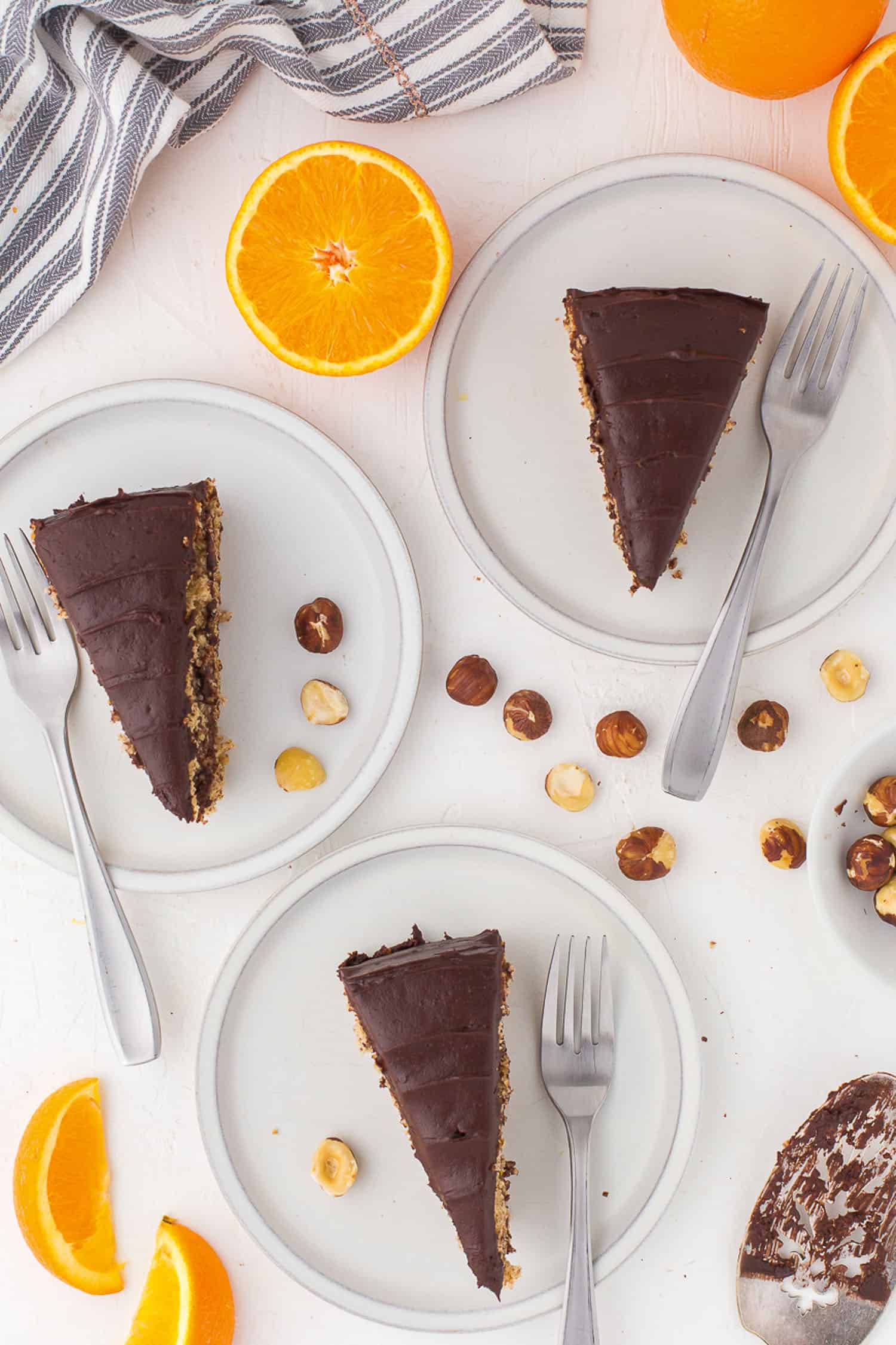 overview of 3 slices of chocolate hazelnut torte with orange slices on white background