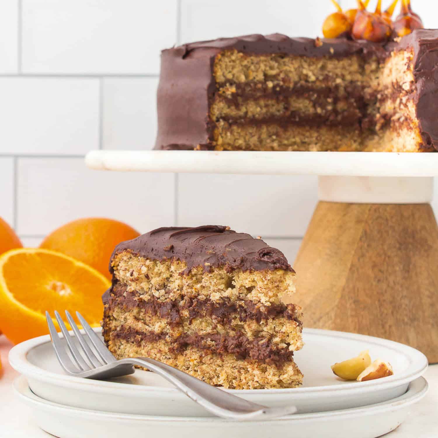 Hazelnut torte slice on a dish with torte in the background on a cake pedestal. 