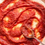 pizza dough being spread with pizza sauce