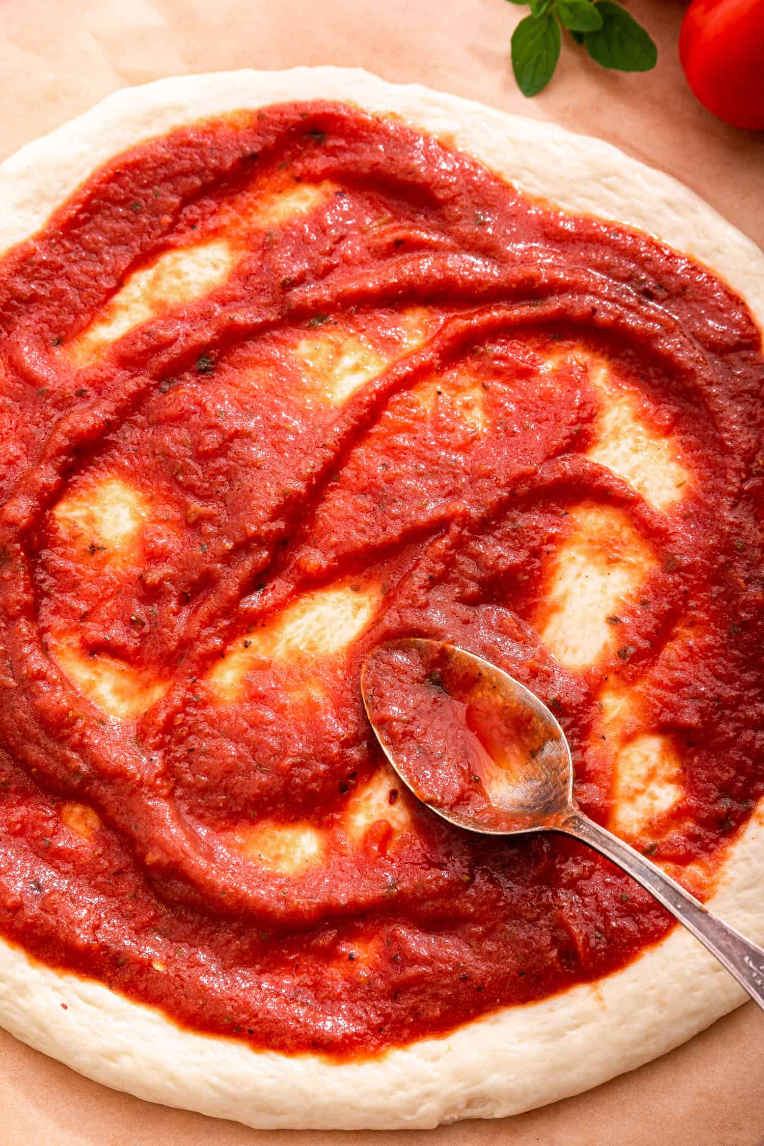 pizza dough being spread with pizza sauce