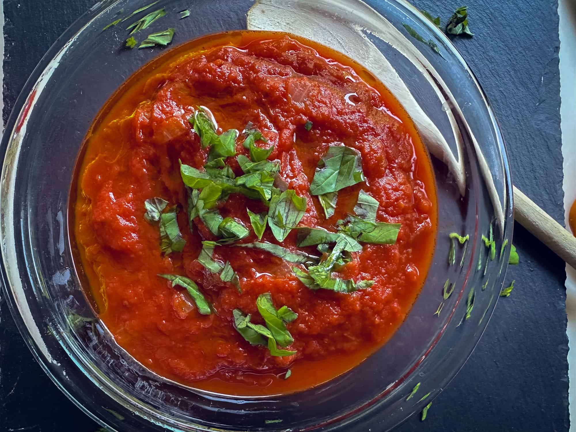 marinara sauce with basil in glass bowl with wooden spoon