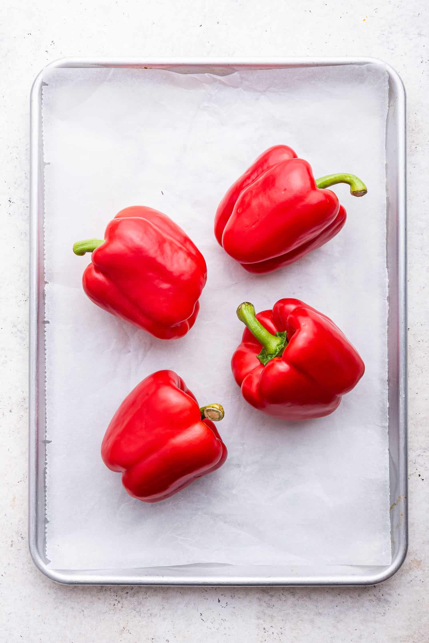 four red bell peppers on parchment lined baking sheet