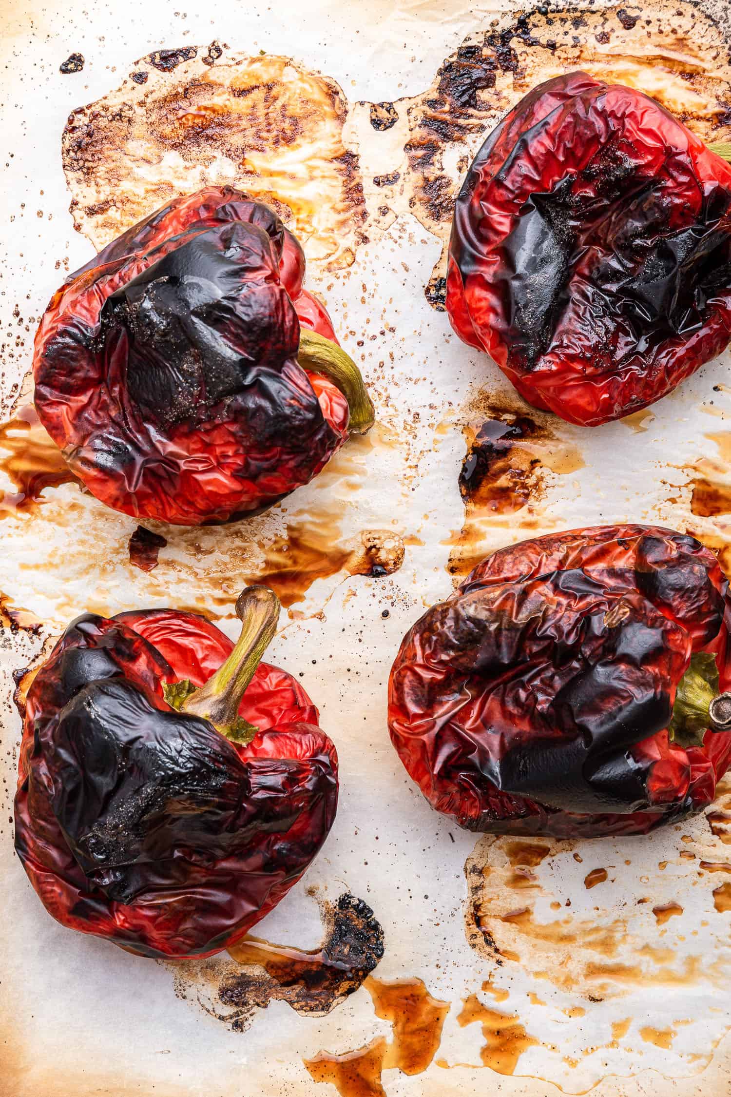 charred red bell peppers on parchment ready for steaming and peeling