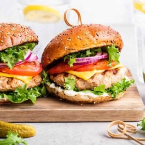 side view of two turkey burgers dressed with cheese, tomato, onion and lettuce, on wooden cutting board