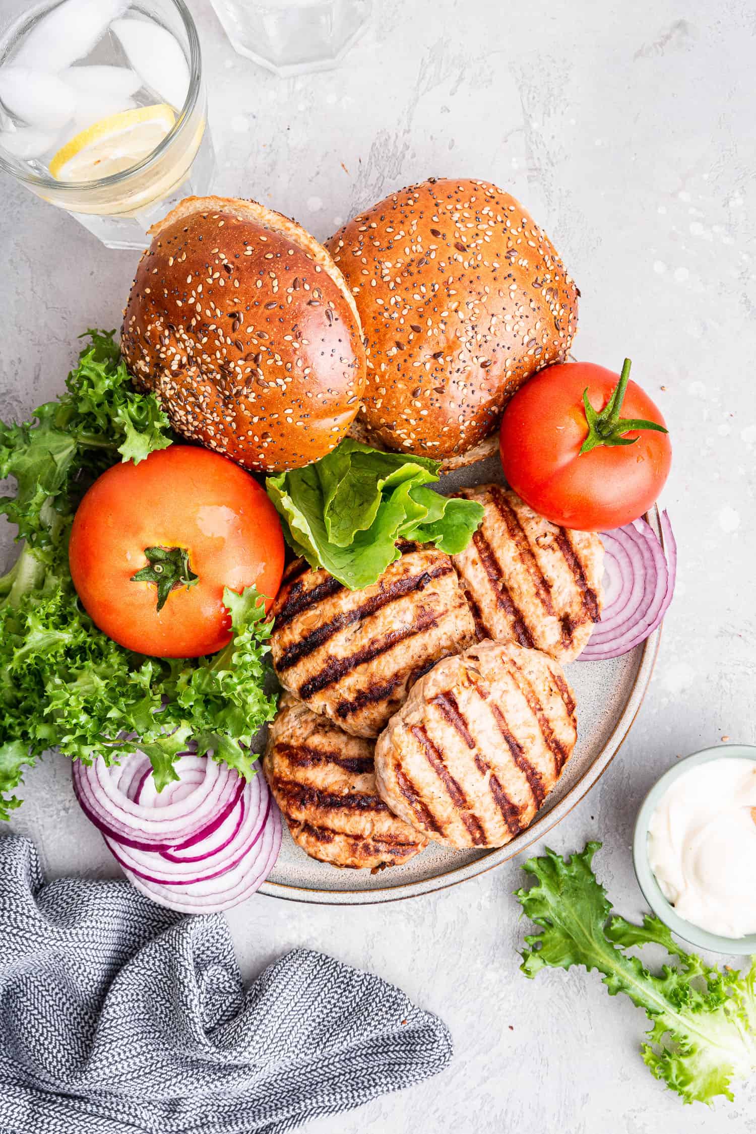 white plate of turkey burgers with toppings and buns for serving
