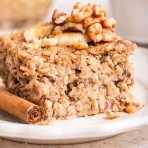 close up side view of baked oats on white plate with nuts and cinnamon stick