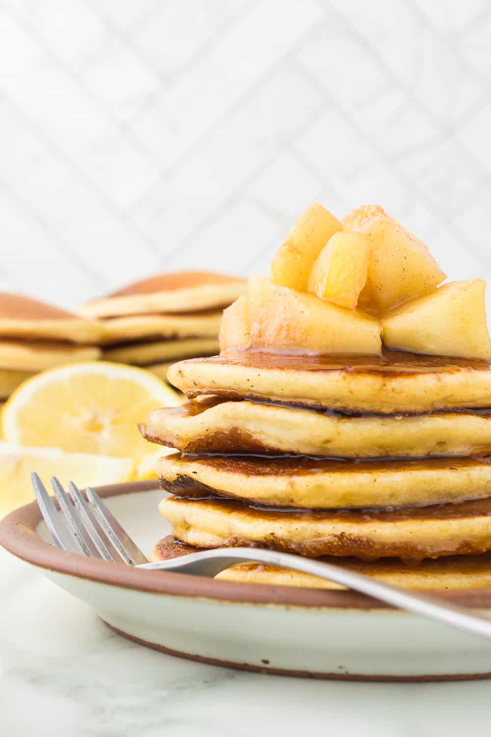 side view of pancakes stacked on plate with fork topped with apples and syrup