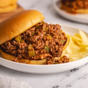 side view of sloppy joe on bun with chips on white plate