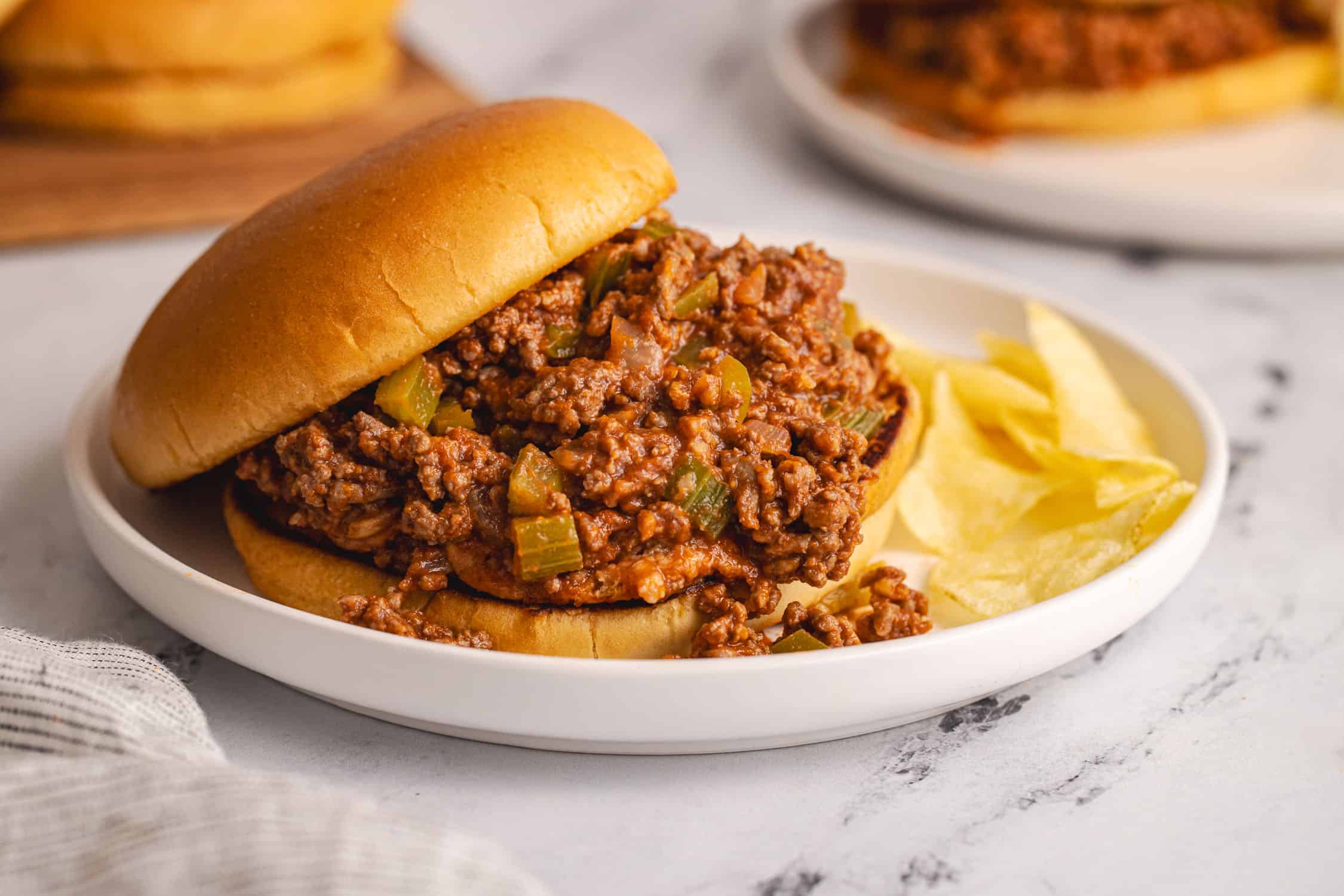 side view of sloppy joe on bun with chips on white plate