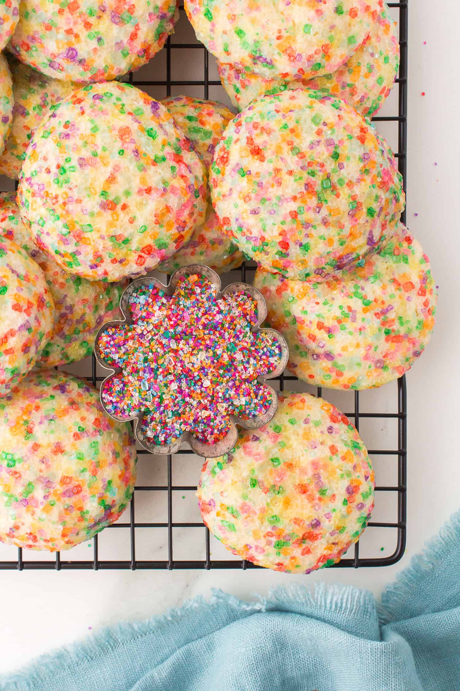 soft sugar cookies piled on wire rack with cup of colored sugar