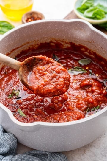 A wooden spoon full of sauce comes out of the pot with extra olive oil.