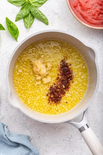 Adding minced garlic and red pepper flake to onion in white pot.