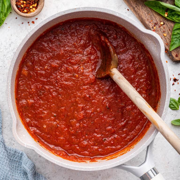 Small white pot full of Arrabbiata sauce with a wooden spoon.