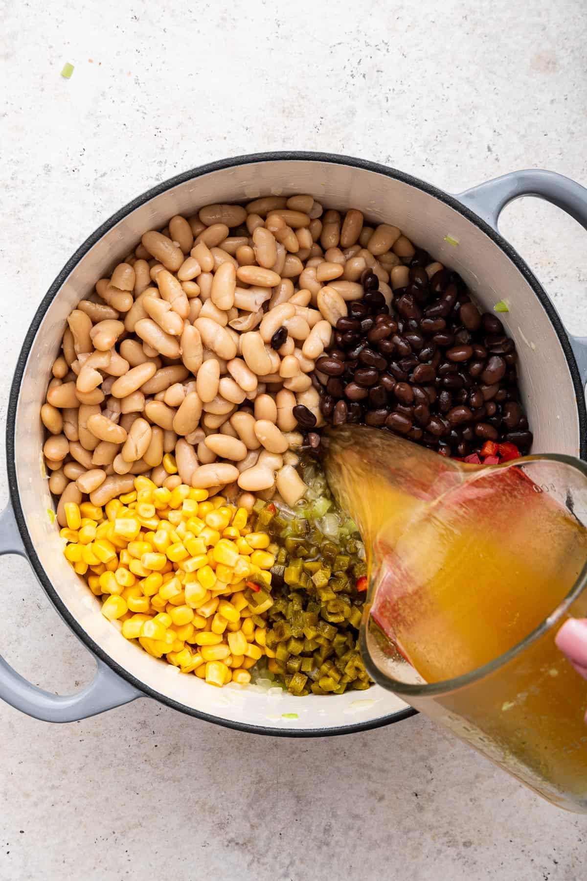 Adding chicken broth to the beans, peppers and corn.