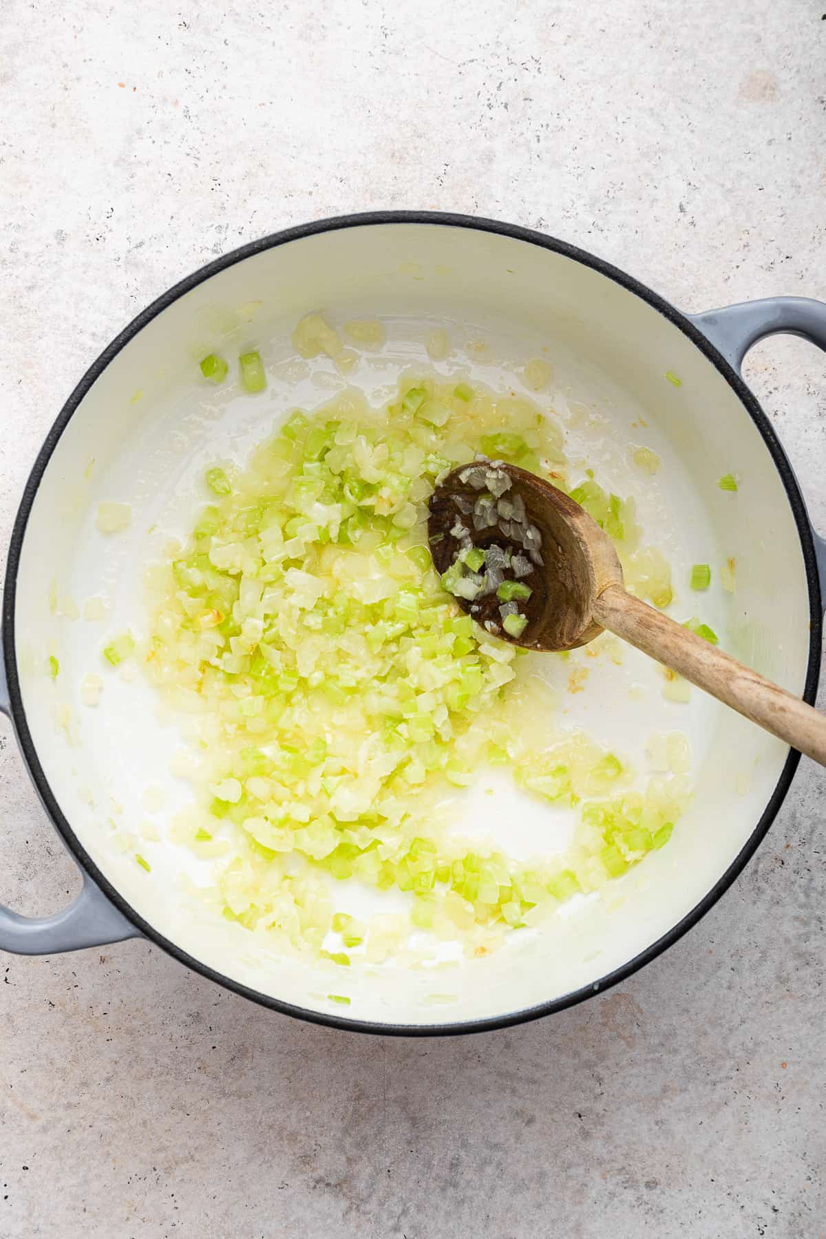 Sauteeing the celery, garlic, and onions in a large pot with a wooden spoon,