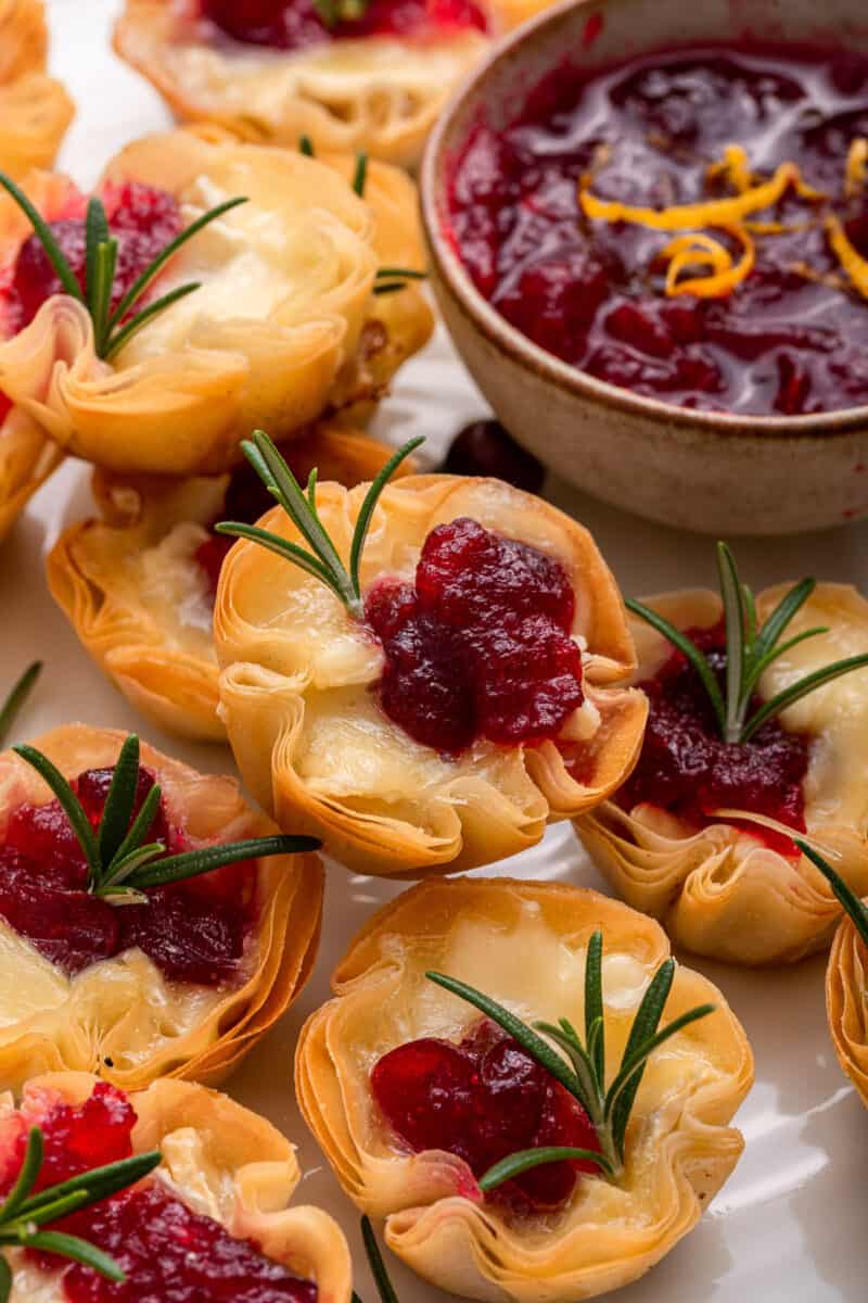 Cranberry brie bites with rosemary and a bowl of cranberry sauce.