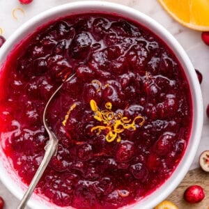 Bowl of homemade cranberry sauce with orange zest and spoon.