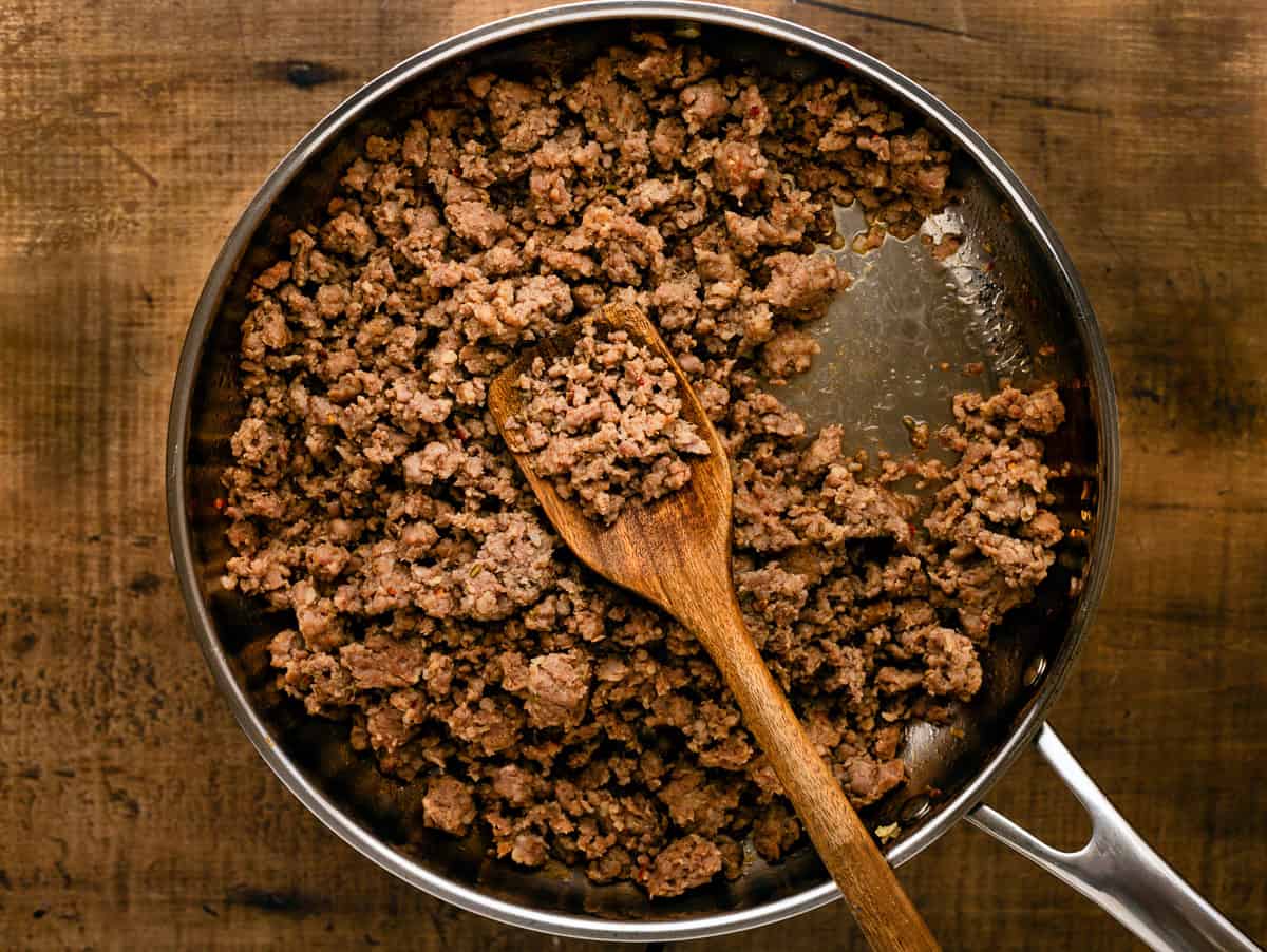 Sauteeing Italian sausage crumbles in pan with wooden spoon.