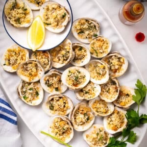 Baked clams with lemon and parsley in white tray.