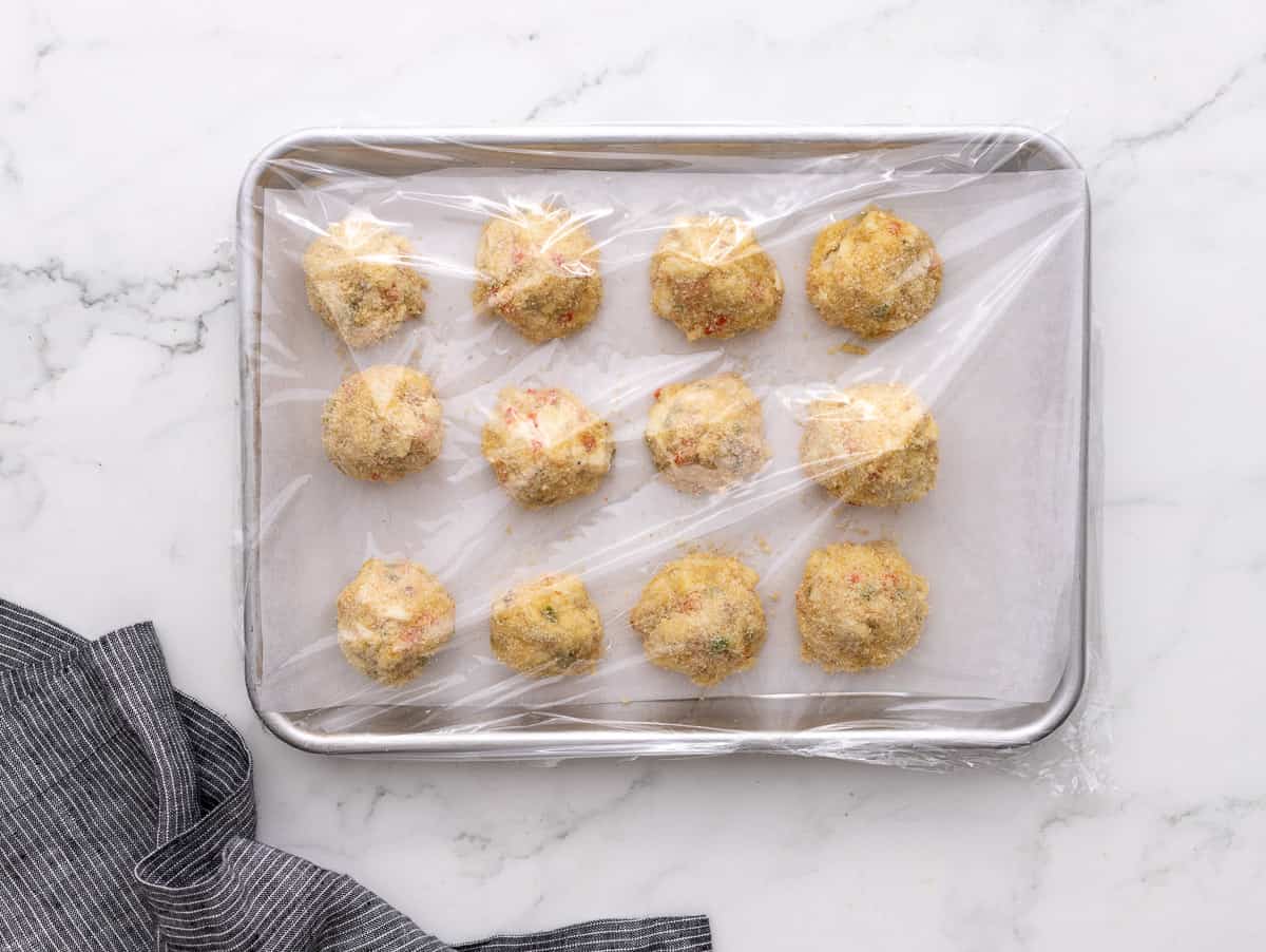 Crab balls on baking sheet covered with plastic wrap.
