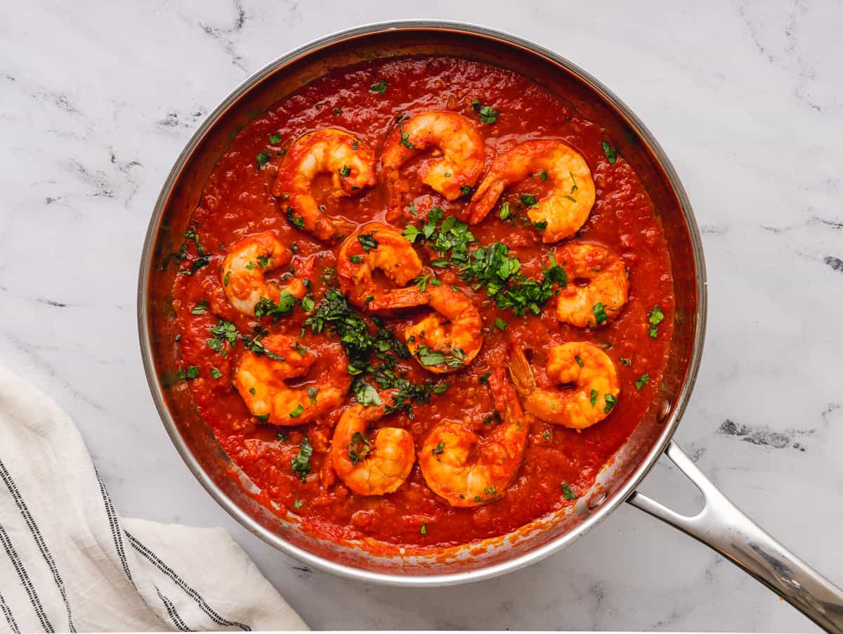 Topping shrimp fra diavolo sauce in pot with parsley.