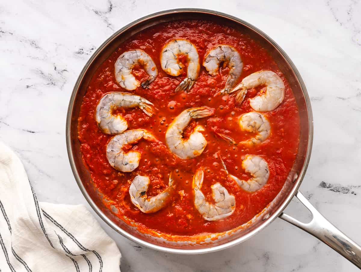 Raw shrimp added to pot of tomato sauce.