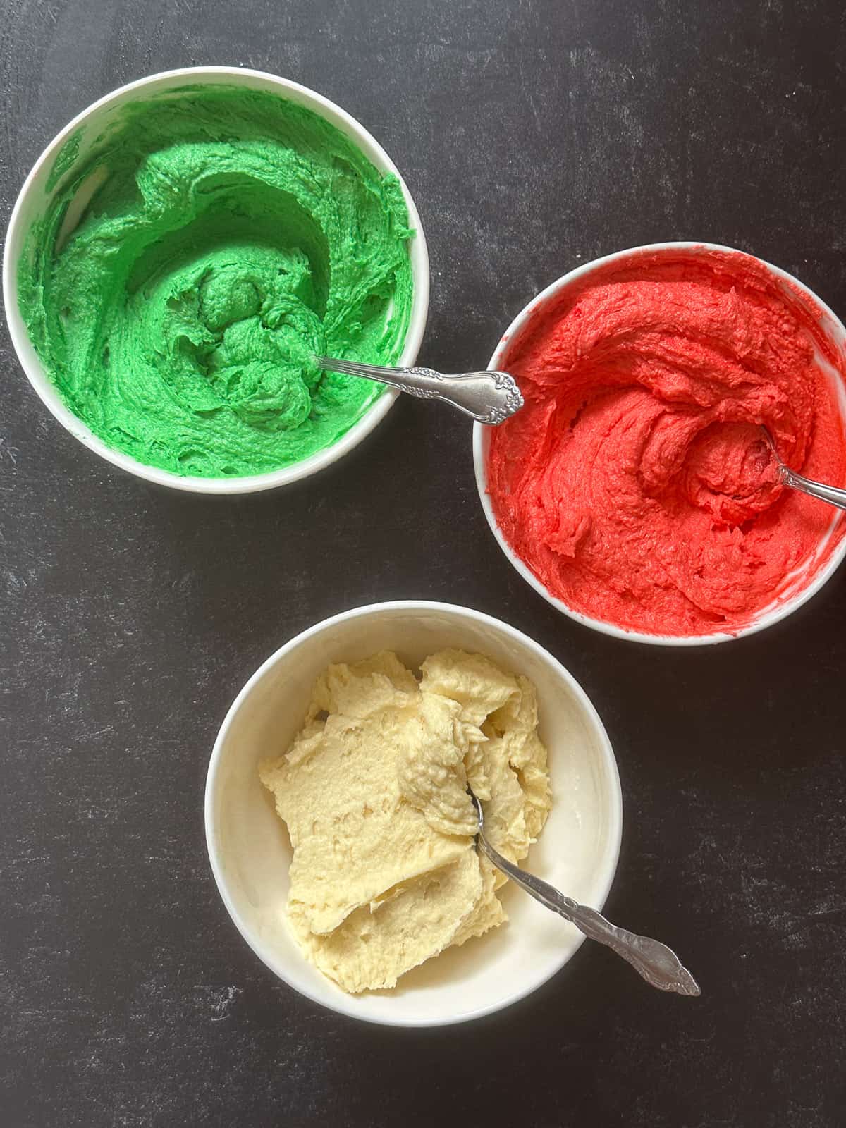 Three bowls of cake batter in green, white, and red.