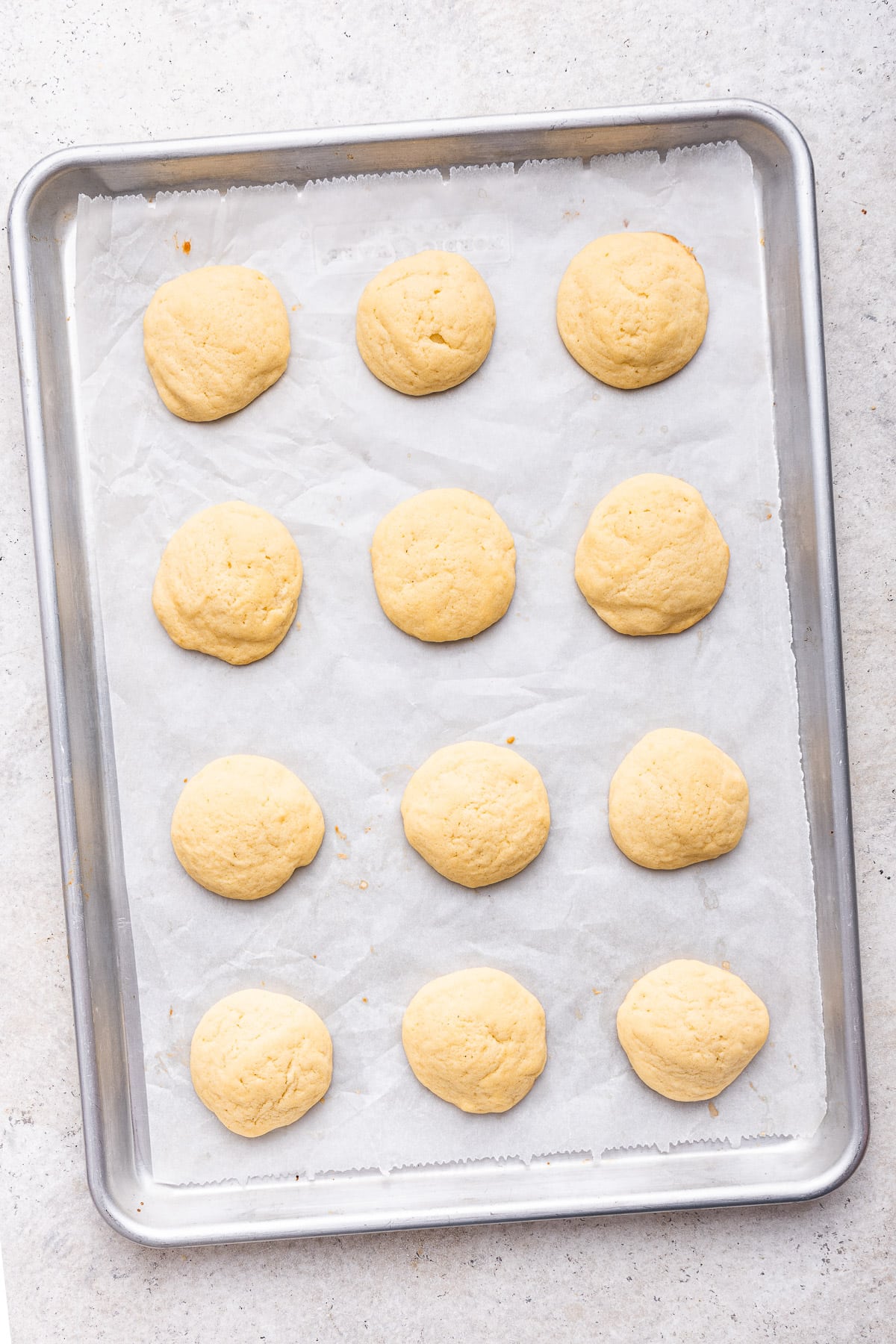 Tray of baked lemon ricotta cookies on parchment lined cookie sheet.