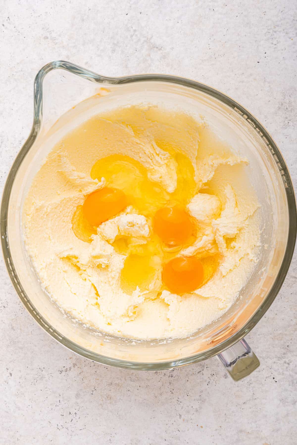 Adding eggs to the batter in a glass bowl.