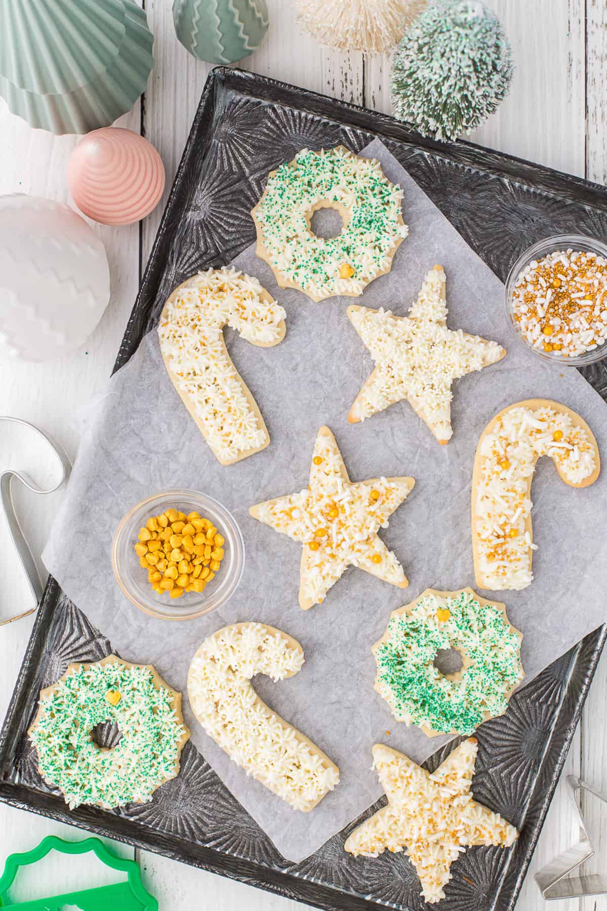 A tray with parchment paper and decorated Christmas cookies with cups of sprinkles.