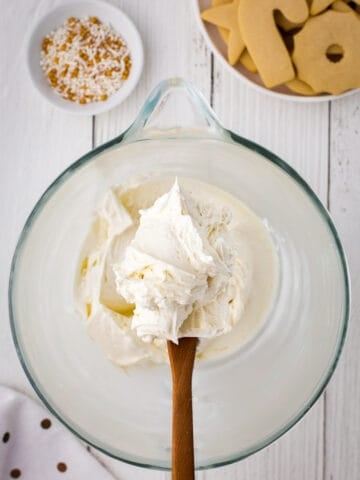 A spatula with buttercream cookie frosting over a glass bowl.
