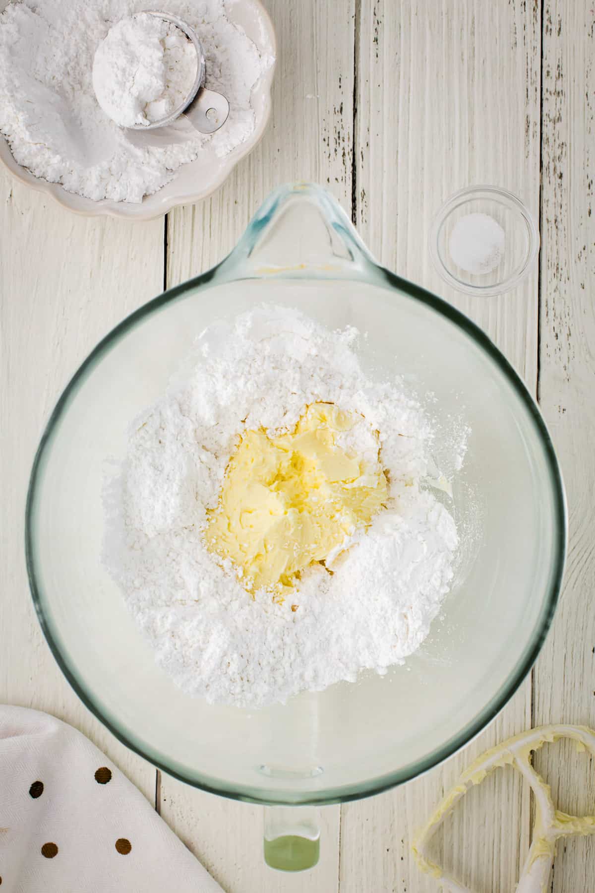 Adding powdered sugar to whipped butter in a glass bowl.