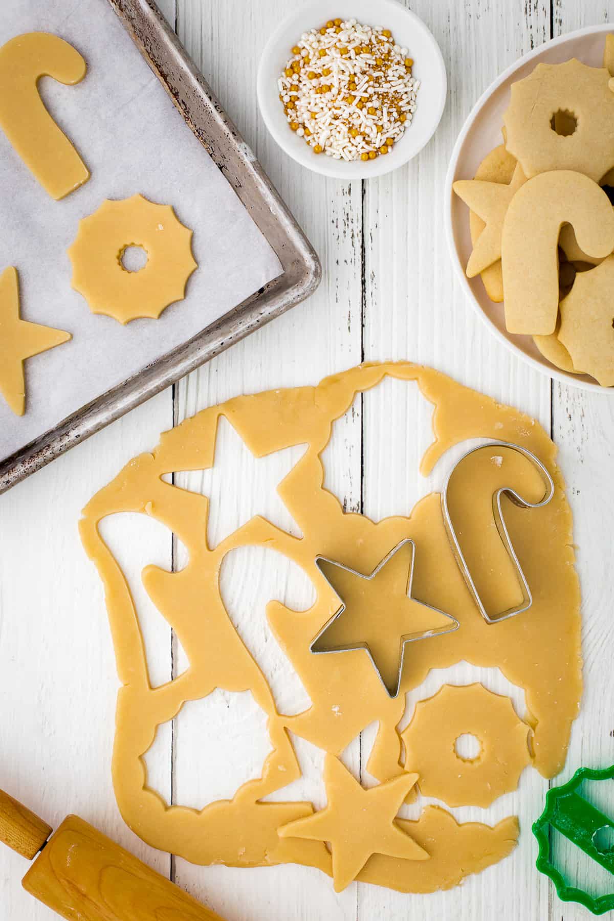 Cutting cookies from rolled-out dough with star and candy cane shapes.