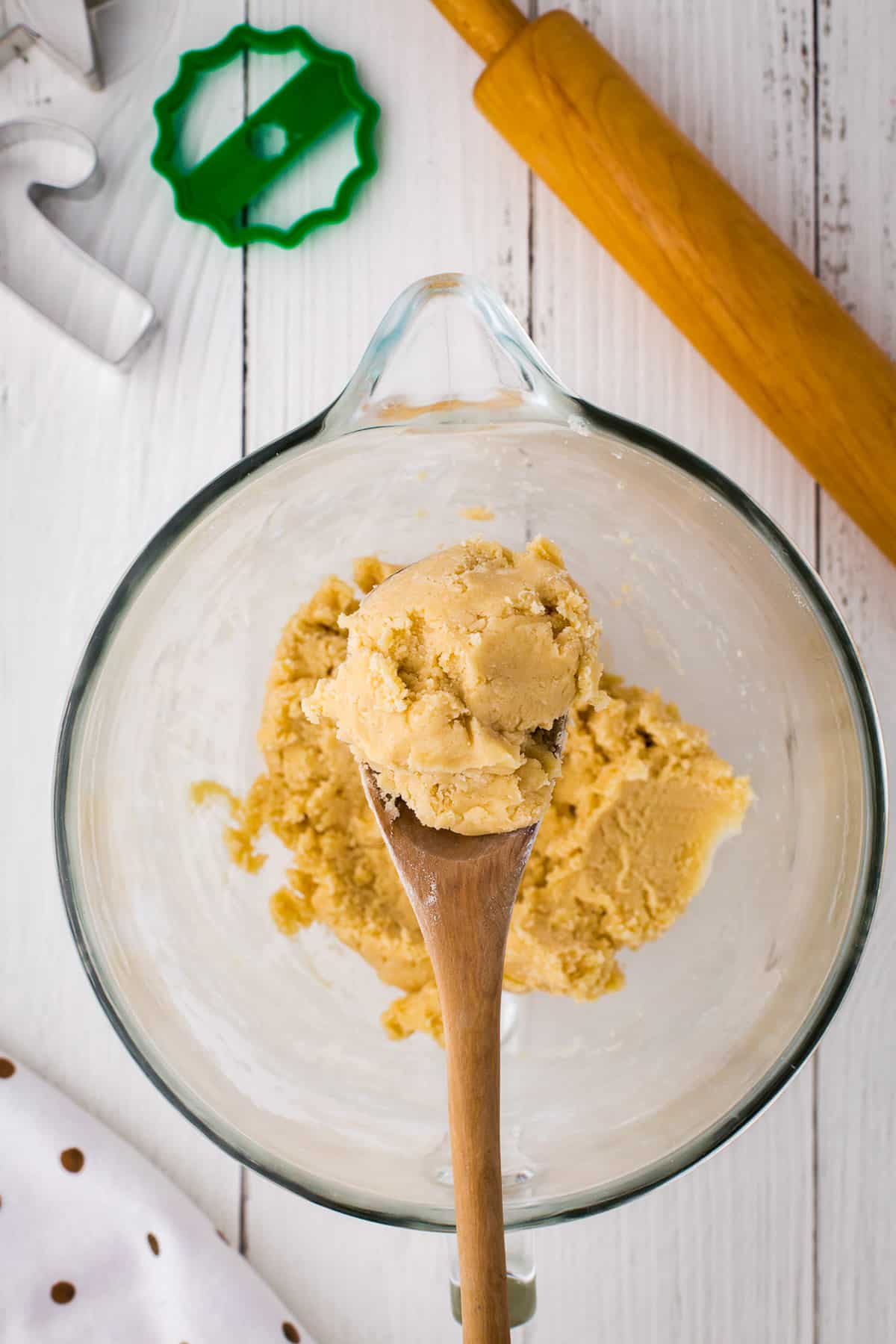 Wooden spoon full of dough hovering over a glass bowl full of cookie dough.