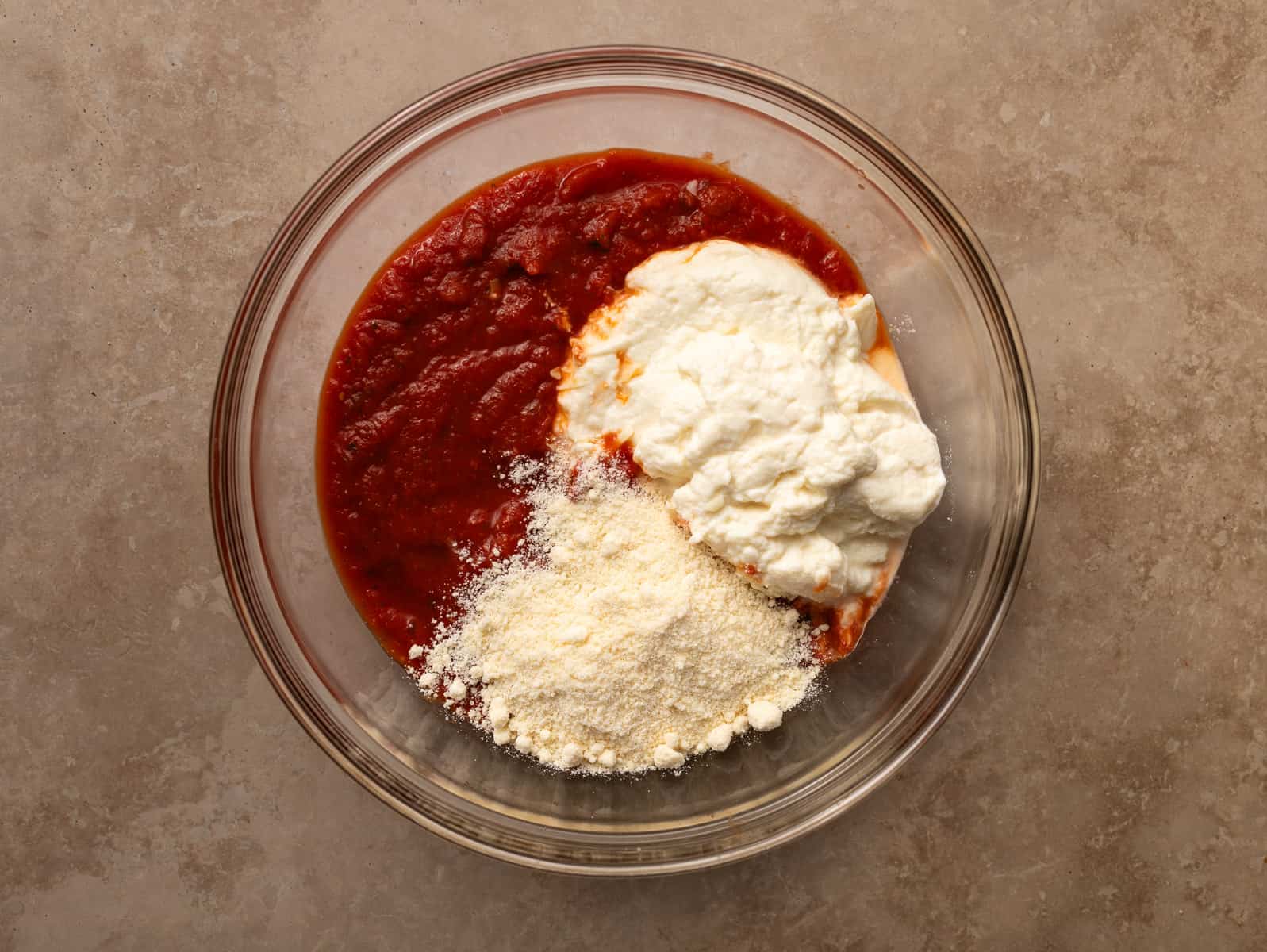 Glass bowl with sauce, ricotta, egg and cheese.
