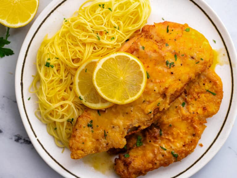 Chicken francaise with lemon and spaghetti on white plate.