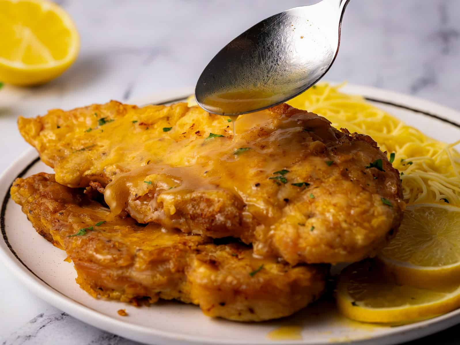 Chicken Francaise with pasta on white plate with spoon drizzling sauce.