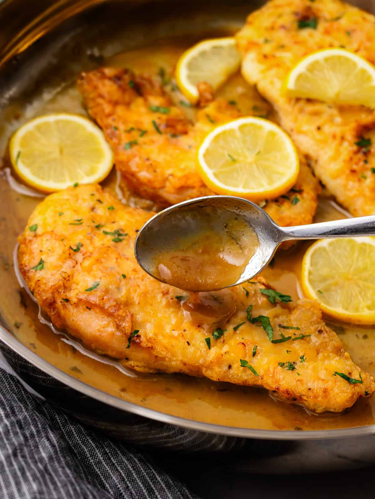 Chicken Francaise in pan with sliced lemon and pan sauce.
