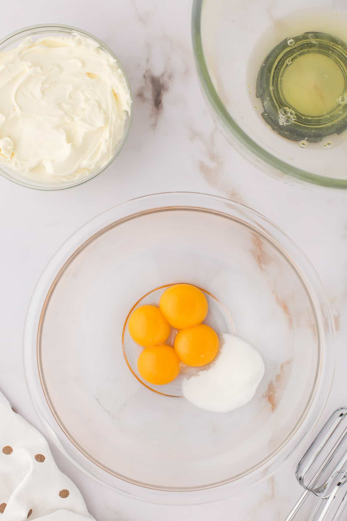 Egg yolks and sugar in glass bowl.