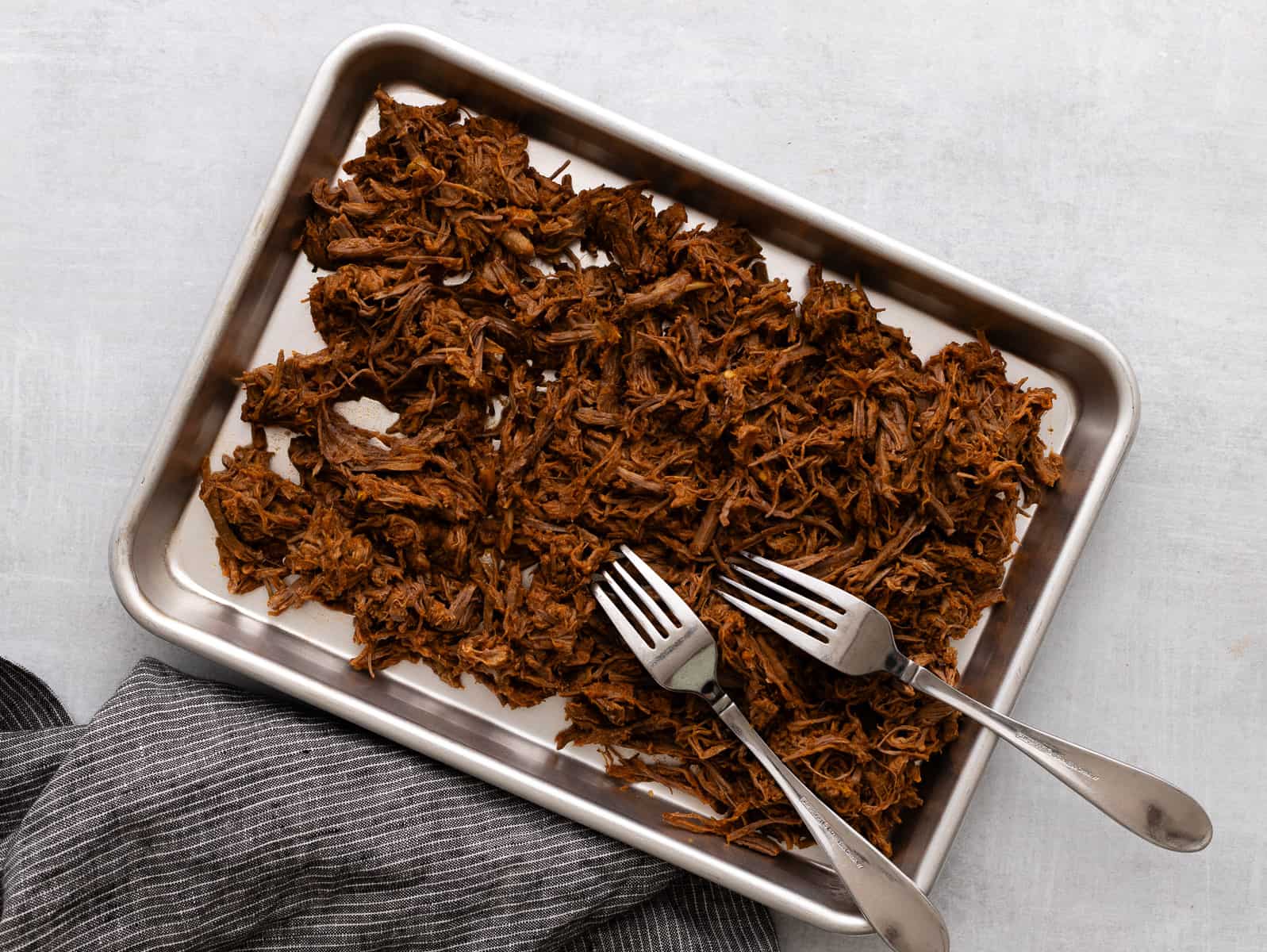 Shredded beef on a baking sheet with forks.